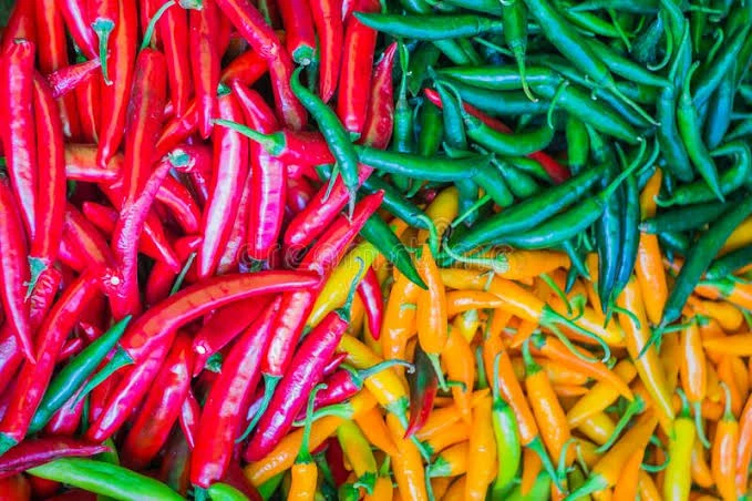 A bowl of chilli flakes surrounded by fresh red chillies